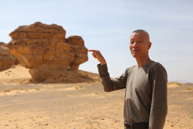 Cai Guo-Qiang posing with a rock in Mada'in Saleh, Saudi Arabia, 2013 Photo by Shu-Wen Lin, courtesy Cai Studio